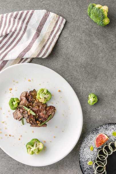 top view of broccoli and fried meat on white plate and fig with onion on black plate - Fotoğraf, Görsel