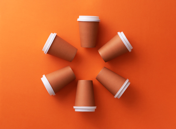 Multiple disposable coffee cups organized in a circle orange background - Photo, Image