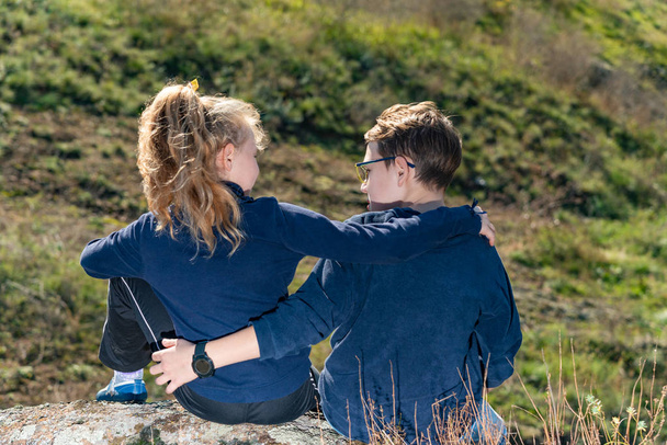 Een jongen met een meisje zitten op een klif, twee vrienden, een broer en zus in een omhelzing zitten en kijken naar elkaar - Foto, afbeelding