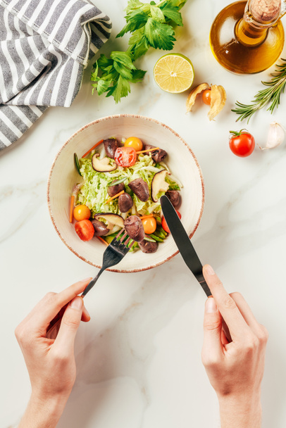 partial view of woman eating salad with fork and knife  - Foto, Bild