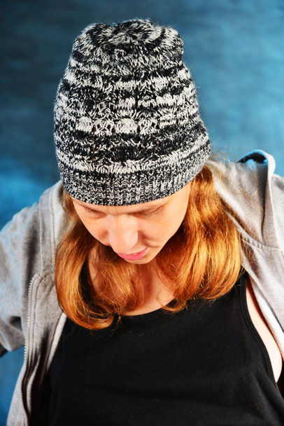 Portrait d'une fille aux cheveux roux dans un chapeau gris tricoté en studio, sur fond bleu
 - Photo, image