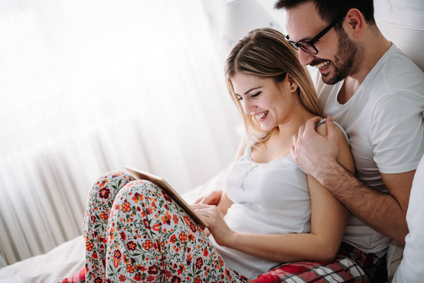 Young happy couple using digital tablet in bedroom - Фото, изображение