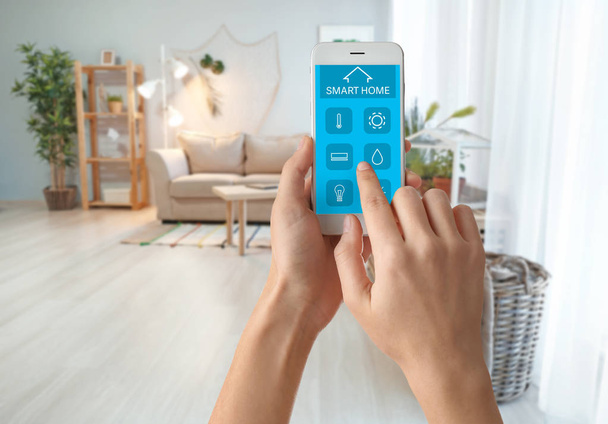 Frau nutzt Handy-Anwendung der Smart-Home-Automation im Zimmer - Foto, Bild
