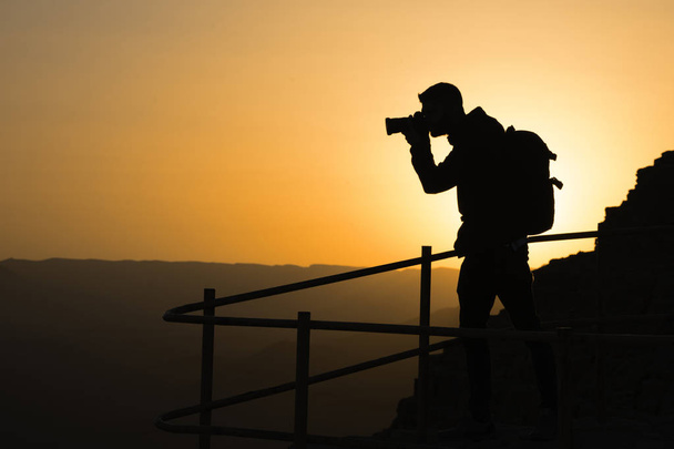 Silhouette of a unrecognizable photographer who shoots a sunset in the mountains. Photographer concept - Fotó, kép