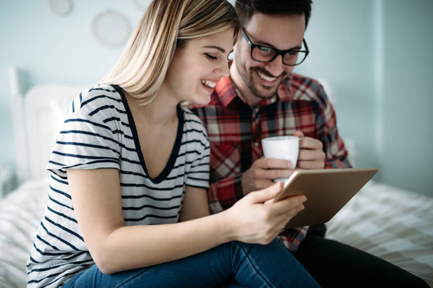 Young happy couple using digital tablet in bedroom - Foto, afbeelding
