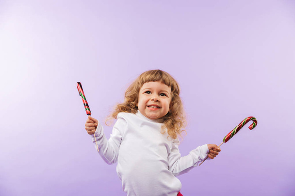 Cheerful little girl holding Christmas lollipop isolated over violet background - Valokuva, kuva