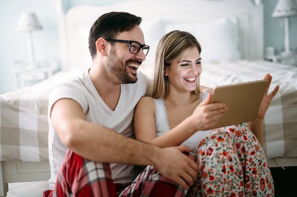 Young happy couple using digital tablet in bedroom - Valokuva, kuva