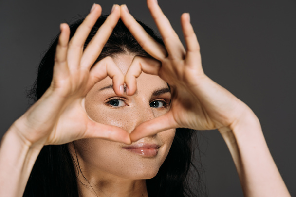 όμορφη γυναίκα τρυφερή δείχνει σημάδι καρδιά που απομονώνονται σε γκρι - Φωτογραφία, εικόνα