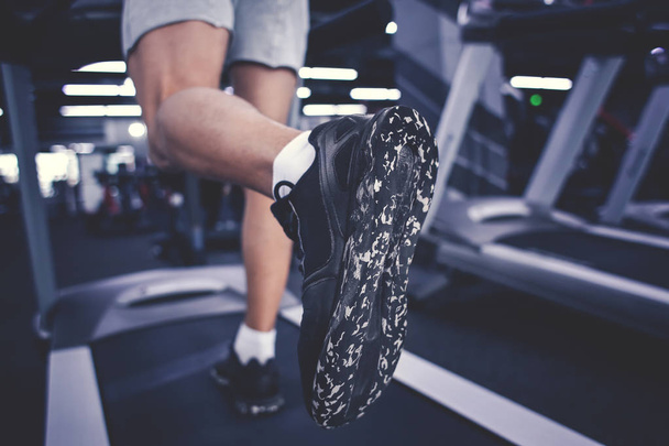 junger sportlicher Mann trainiert auf Laufband in modernem Fitnessstudio, Nahaufnahme - Foto, Bild