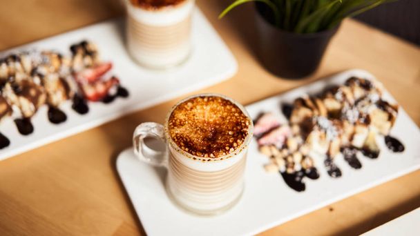 Banner size of two cups of Hot latte with baked caramel crust and sweet roll with banana and strawberry on the wooden table in coffe-shop. Coffee concept. - Foto, immagini