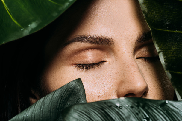 красивая женщина с закрытыми глазами позирует с зелеными пальмовыми листьями
 - Фото, изображение