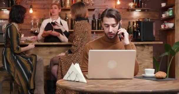 Joven freelancer conversando por teléfono en un restaurante concurrido. Trabajando en su computadora. Gestión de su negocio en línea
 - Metraje, vídeo