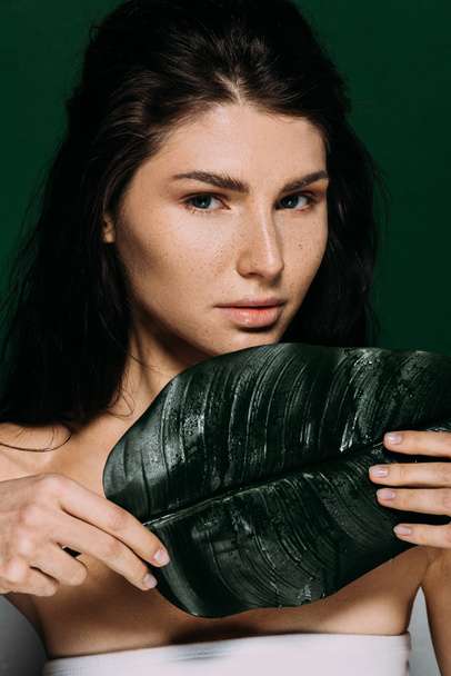 Portret van mooi meisje bedrijf groene palmtak geïsoleerd op groen - Foto, afbeelding
