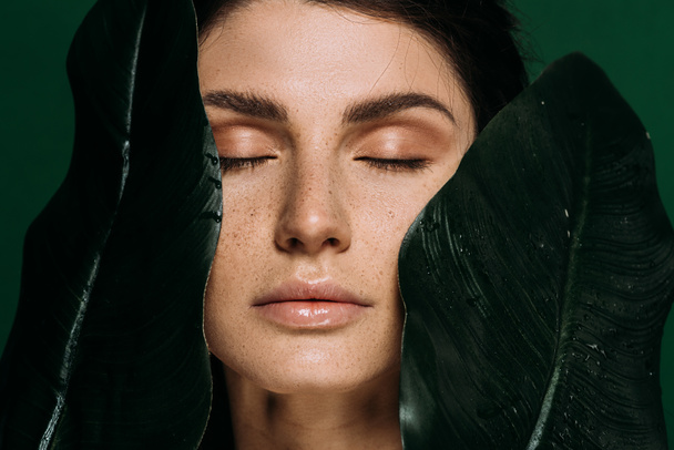 Retrato de hermosa chica con los ojos cerrados posando con hojas verdes aisladas en verde
 - Foto, imagen