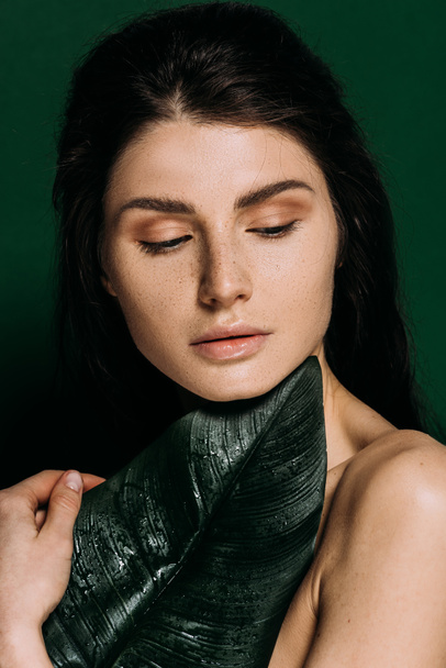 Portrait of beautiful woman with freckles on face posing with palm leaf isolated on green - Foto, immagini