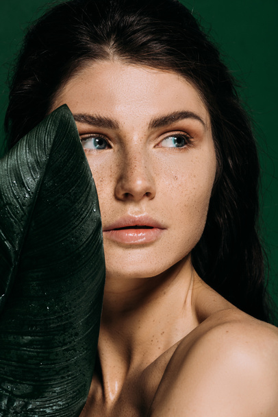 Portrait of beautiful girl with freckles on face posing with leaf isolated on green - Foto, afbeelding