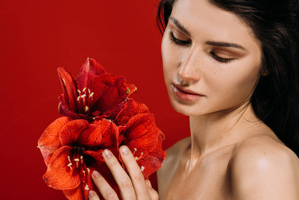 Porträt einer zarten jungen Frau, die Amaryllis-Blumen betrachtet, isoliert auf Rot - Foto, Bild