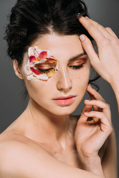tender brunette girl with floral petals around eye isolated on grey - Foto, Imagen