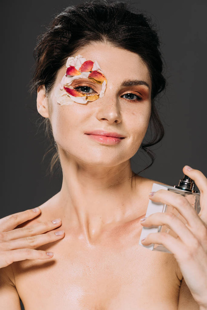 Portrait of young woman with petals on face spraying perfume isolated on grey - Foto, Bild