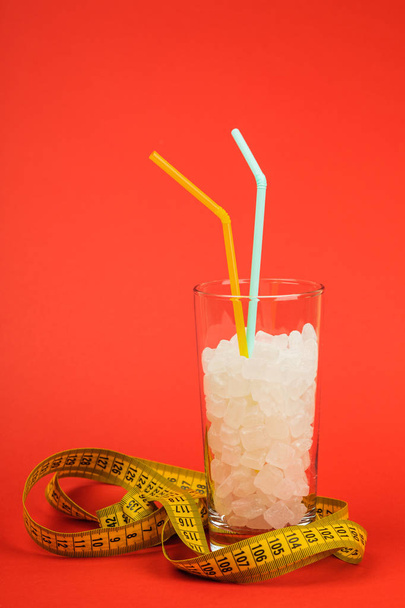 Ένα ποτήρι ζάχαρη σε κύβους, είναι μια έννοια των ανθυγιεινών τροφίμων. Σε κόκκινο φόντο. - Φωτογραφία, εικόνα