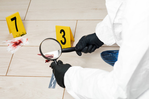Expert criminology through a magnifying glass looking at a bloody knife at the crime scene. - Фото, зображення