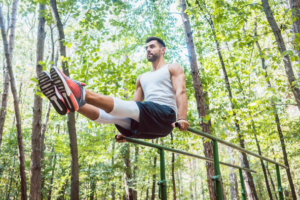 Fit man doing abdominal exercises in forest outdoor gym  - Photo, Image