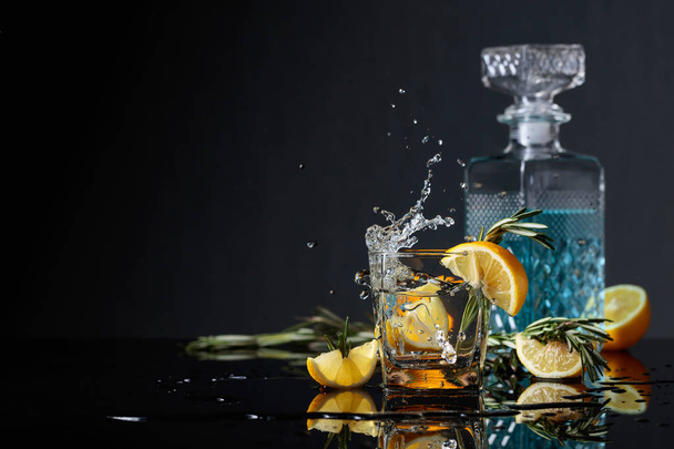 Koktél gin-tonic, citromos szelet, és rozmaring ágakkal. Citromos szelet esik a pohárba. Másolja a hely. - Fotó, kép
