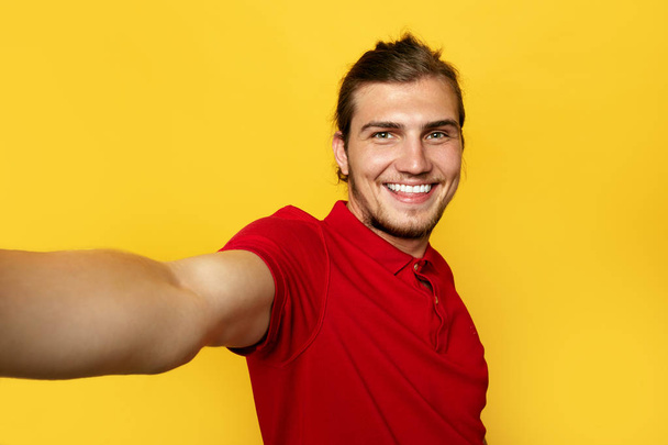 Εσωτερικη πορτρέτο του ένα χαρούμενο γενειοφόρος άνδρας λαμβάνοντας αυτοπορτρέτα πάνω από το κίτρινο φόντο. - Φωτογραφία, εικόνα
