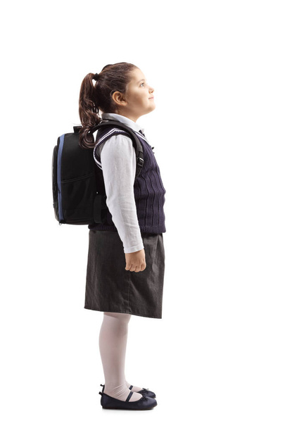 Full length profile shot of a little schoolgirl in a uniform looking up isolated on white background - Foto, Bild