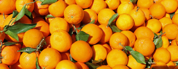 achtergrond van veel rijpe sinaasappels met bladeren op markt - Foto, afbeelding