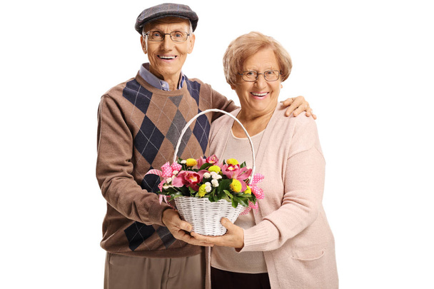 Elderly man and woman holding a basket with flowers and smiling at the camera isolated on white background - Zdjęcie, obraz