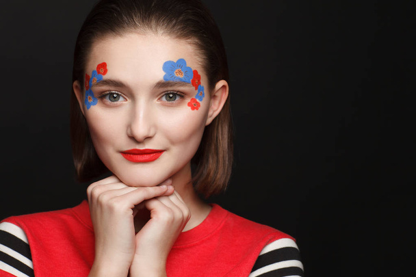 Photo of a young girl with makeup in the form of flowers in red and blue. Black background - Valokuva, kuva