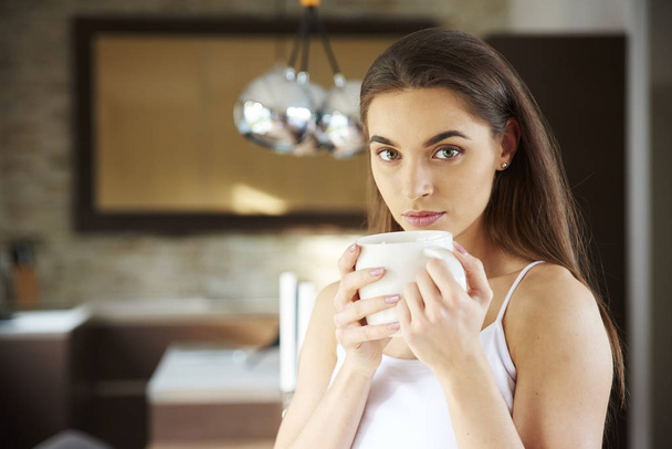 Portrait shot of happy woman wearing casual clothes while drinking her morning tea at home.  - Foto, Imagen