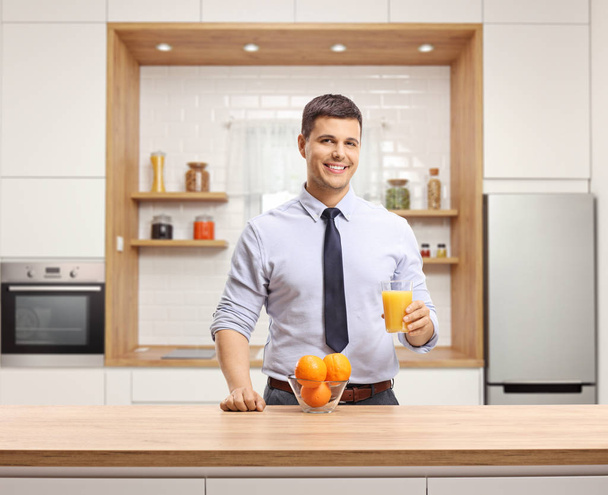Young man dressed for work drinking orange juice in a modern kitchen  - Zdjęcie, obraz