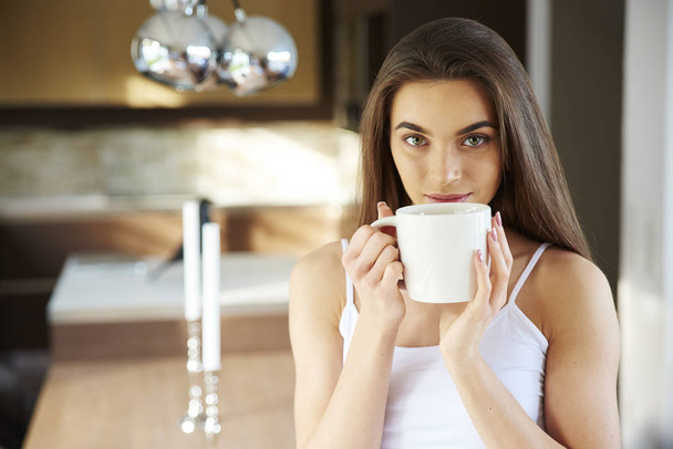 Крупный план портрета молодой женщины в пижаме и пьющей утренний чай, расслабляясь дома на диване
.  - Фото, изображение