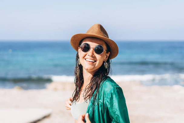Cute pan asian girl in hat and sunglasses in green pareo walking on the seaside - Foto, imagen
