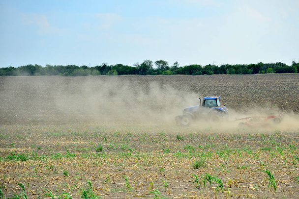 Трактор вспахивает землю и пыль летит в разных направлениях, подготавливая землю к посеву на вёслах
. - Фото, изображение