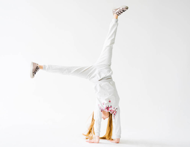 Active little girl on white backgroung doing a handstand - Photo, image