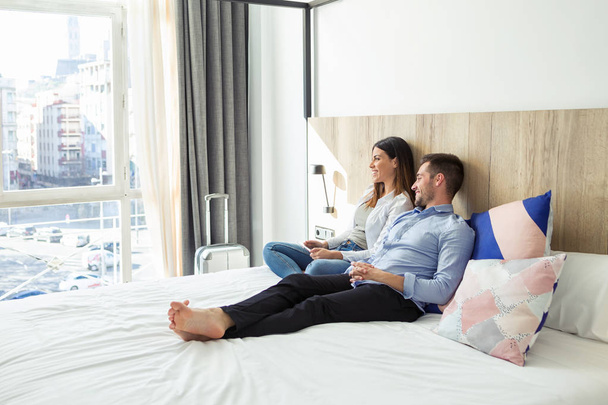 Shot z krásné krásný mladý pár, lhaní a relaxaci na posteli pohlédl stranou na hotelovém pokoji. - Fotografie, Obrázek