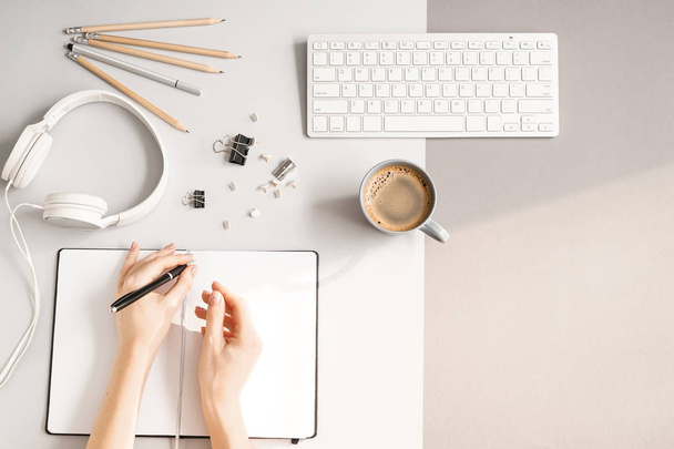 Руки жінки, що пишуть в блокноті, клавіатурі ПК, навушниках і чашці кави на сірому фоні, вид зверху
 - Фото, зображення