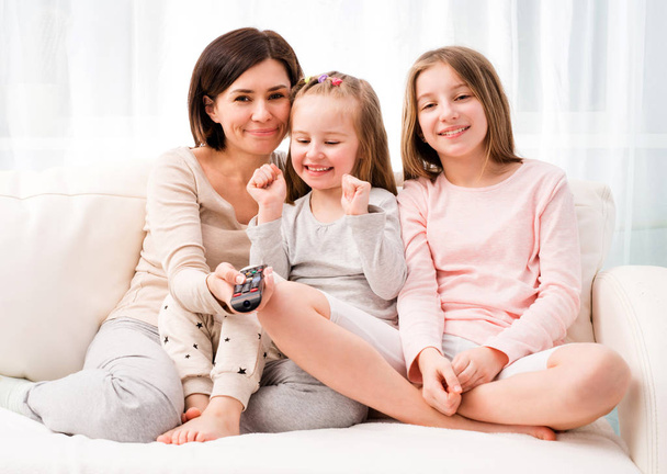 Mom hugging daughters while watching TV at home - Фото, зображення