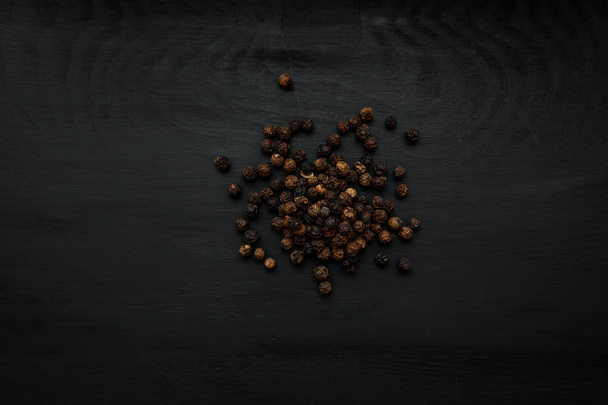 Close-up image of black pepper on black wood background, view above - Foto, Imagem