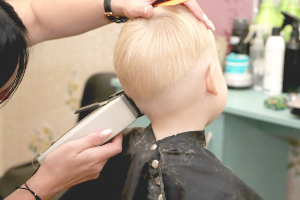 A little boy is cutting a hairdresser in the salon. The kid is watching a cartoon. Green screen on a laptop for signature - Photo, Image