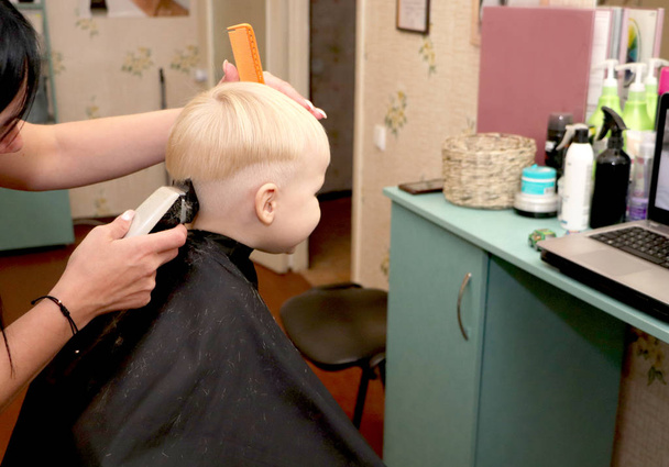 Mały chłopiec jest cięcie fryzjera w salonie. Dziecko jest oglądanie kreskówki. Zielony ekran w laptopie do podpisu - Zdjęcie, obraz