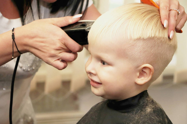 Ein kleiner Junge schneidet im Salon einen Friseur. das Kind schaut sich einen Zeichentrickfilm an. Green Screen auf einem Laptop zur Unterschrift - Foto, Bild