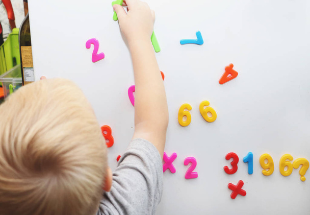 Ένα μικρό αγόρι μελετά το μαγνητικό αριθμούς στο ψυγείο. Preschooler κατάρτισης - Φωτογραφία, εικόνα