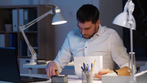 homem de negócios com papéis e laptop no escritório da noite - Filmagem, Vídeo