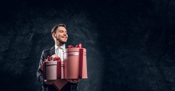elegant gekleideter Mann mit Geschenken, während er in einem dunklen Studio posiert - Foto, Bild