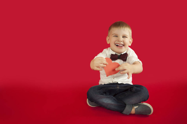 for holidays, lovers day and mothers day, baby boy sits on a red background with a red heart in his hands. The concept is to give gifts and love - Photo, image