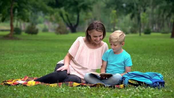 Happy mother and son reading book outdoors, common interest, leisure time - Fotografie, Obrázek